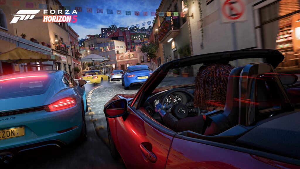 『Forza Horizon 5』のスクリーンショット。メキシコの都市グアナファトの狭いカーブの通りを、カラフルな車に乗ったプレイヤーたちが駆け抜けている