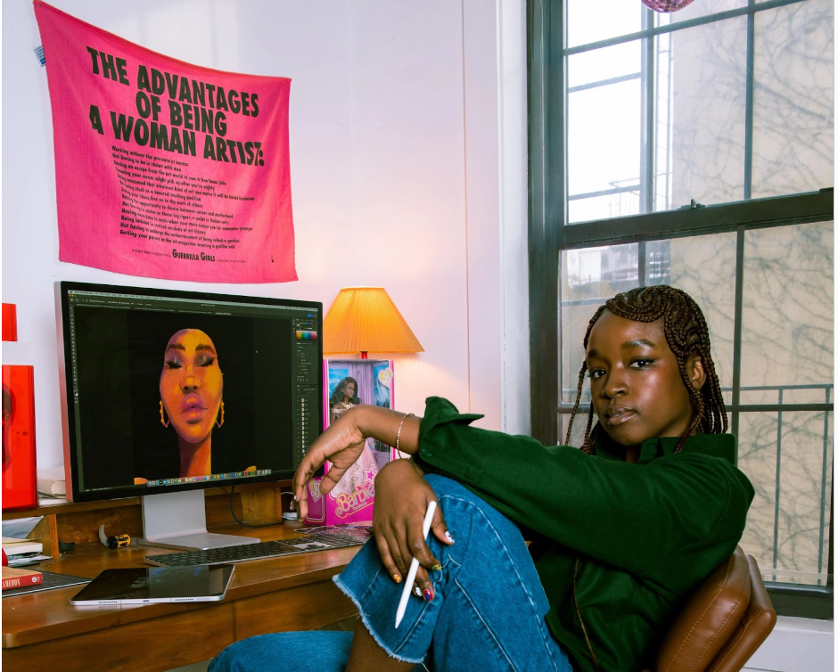 Artist Amika Cooper wearing a green sweater and jeans reclining in a chair at a desk.