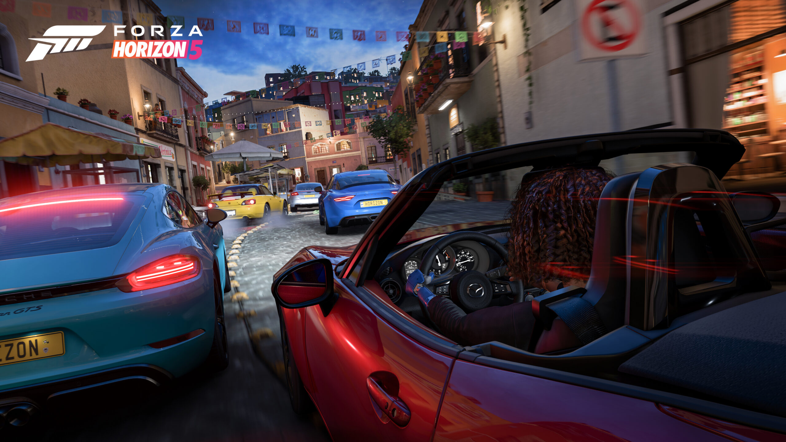 Screenshot from Forza Horizon 5 shows players in a group of colorful cars cruising through a narrow curving street in the city of Guanajuato, Mexico.