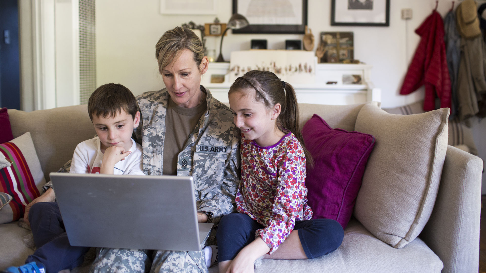 A military service person and two children sit together on a couch while using a laptop together